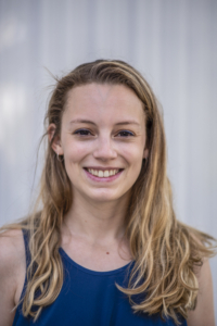 portrait of a young woman smiling with long blond hair wearing a blue tank top on a grey background