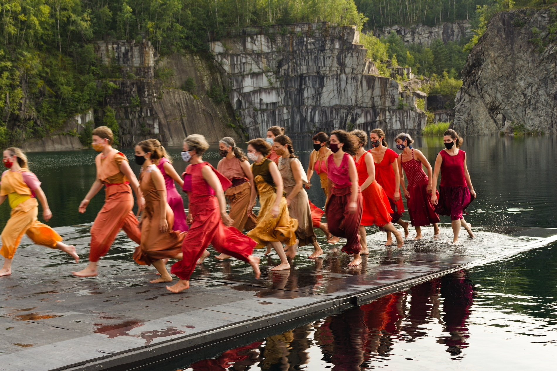 dancers in dressed with clothes in a shade of red running in the same direction on a float in the water filled granite quarry